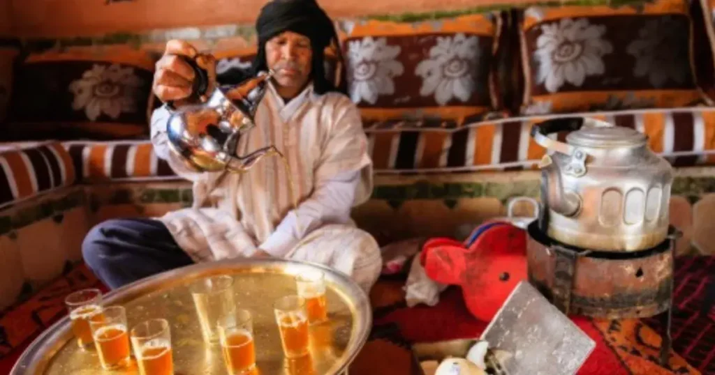 Moroccan man pouring mint tea from height creating traditional reza foam in ornate glass