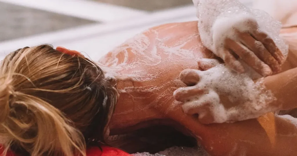 Moroccan hammam attendant performing traditional gommage body scrub exfoliation treatment