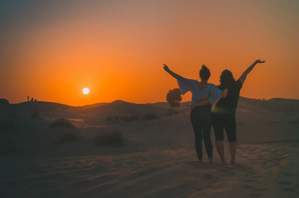 Travelers watching the sunset over dunes, enjoying desert life in Morocco
