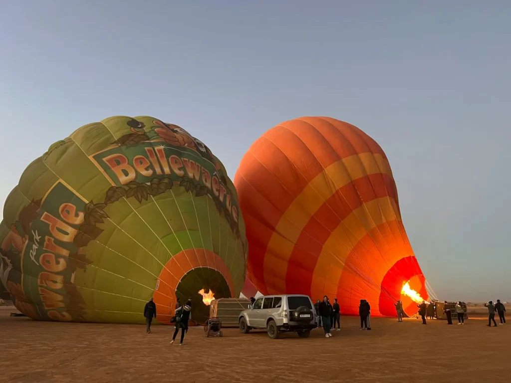 Crew inflating a hot air balloon in Marrakech while guests enjoy morning coffee